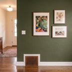 Three framed artworks on a green wall with wooden floor and door in the background