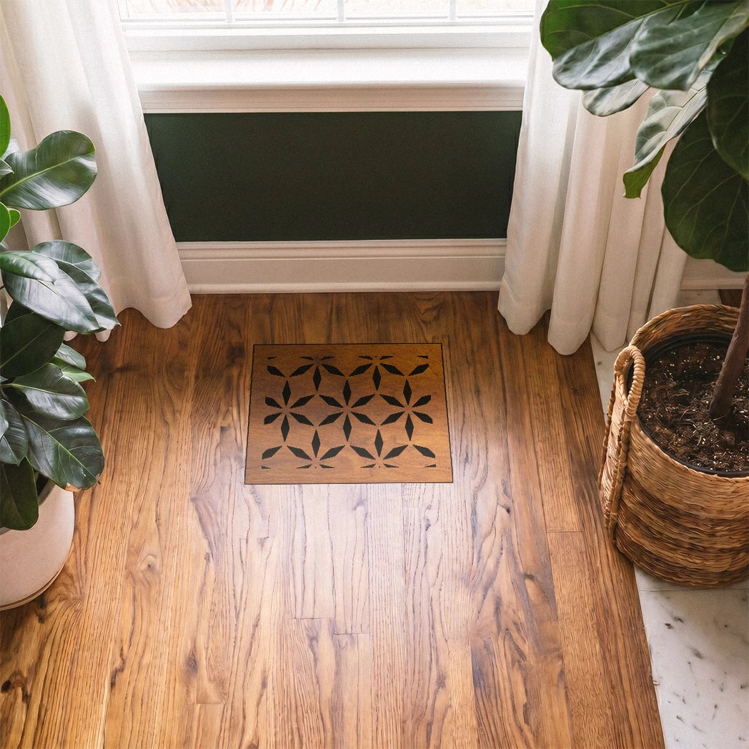 Decorative doormat with geometric pattern on a wooden floor, flanked by potted plants.
