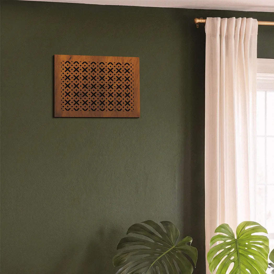 Decorative wooden wall art on a green wall with a window and plant in the background