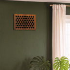 Wooden wall art piece on a green wall with a window and plants in the foreground