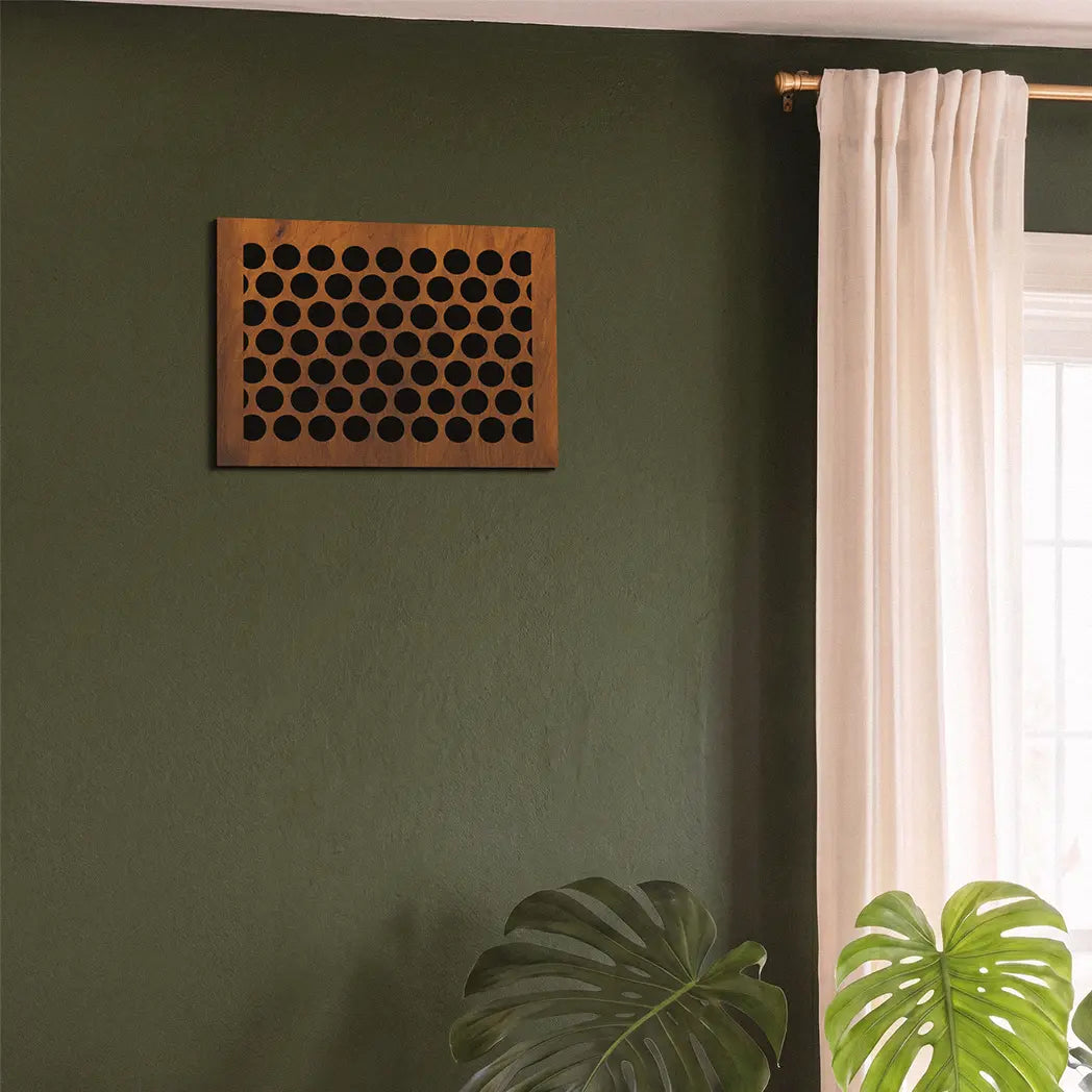 Wooden wall art piece on a green wall with a window and plants in the foreground