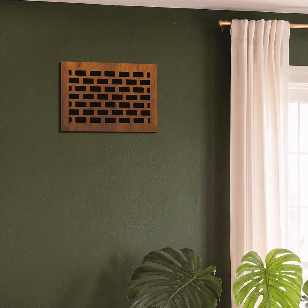 Wooden decorative wall vent on a green wall with a window and plant in the background