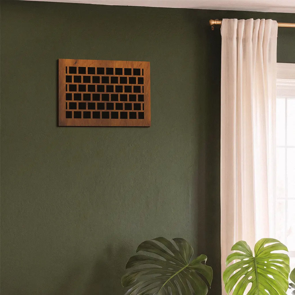 Wooden wall art piece on a green wall with a window and plants in the foreground