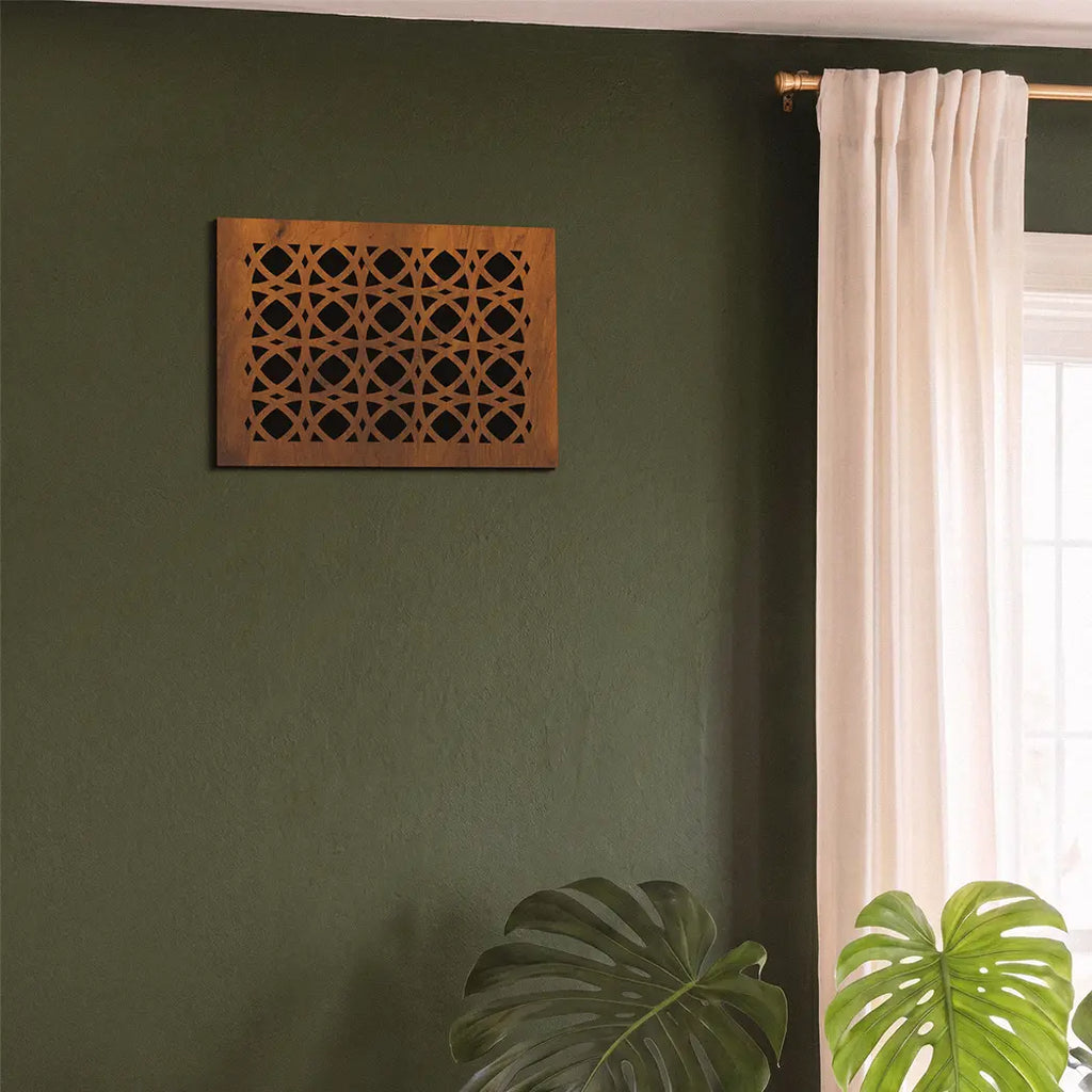 Decorative wooden wall art on a green wall with a window and plant in the background